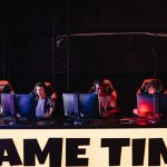 Jogadores participam de um torneio de e-sports em um ambiente interno com iluminação colorida.