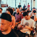 Participantes de diferentes perfis acompanham uma conferência e conversam em um ambiente moderno.
