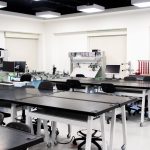 Sala de aula universitária contemporânea com computadores, estações de trabalho e equipamentos tecnológicos.