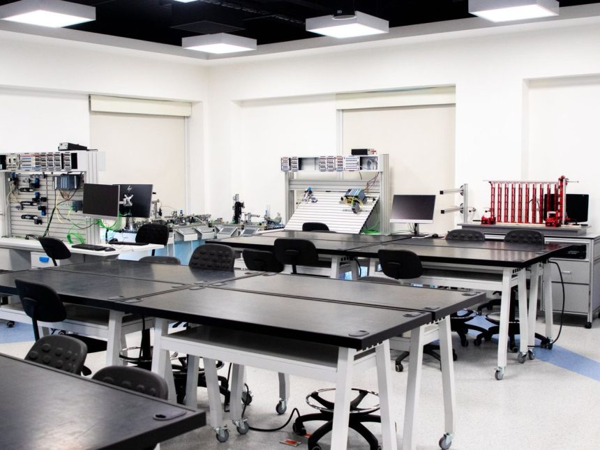 Sala de aula universitária contemporânea com computadores, estações de trabalho e equipamentos tecnológicos.