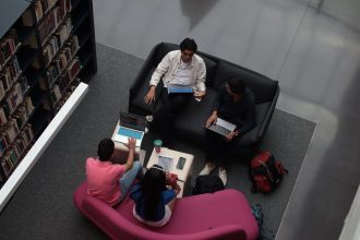 Grupo diverso de adultos colaborando com laptops em uma área de convivência de uma biblioteca.