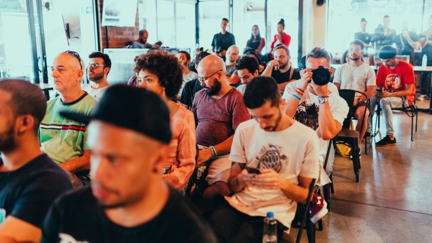 Participantes de diferentes perfis acompanham uma conferência e conversam em um ambiente moderno.