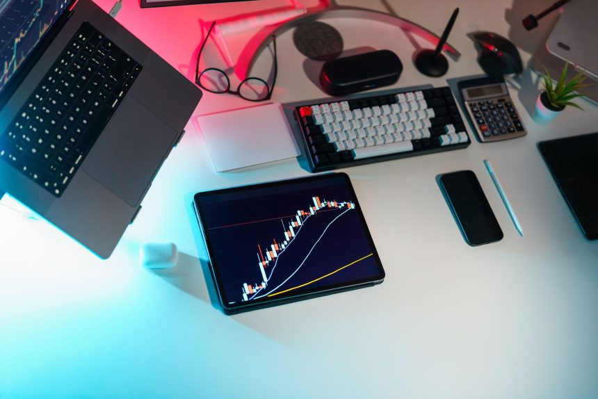 Mesa de escritório com dispositivos digitais exibindo análises financeiras.