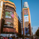 Cena urbana durante o dia, com painéis digitais de publicidade e edifícios ao redor.