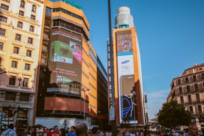 Cena urbana durante o dia, com painéis digitais de publicidade e edifícios ao redor.